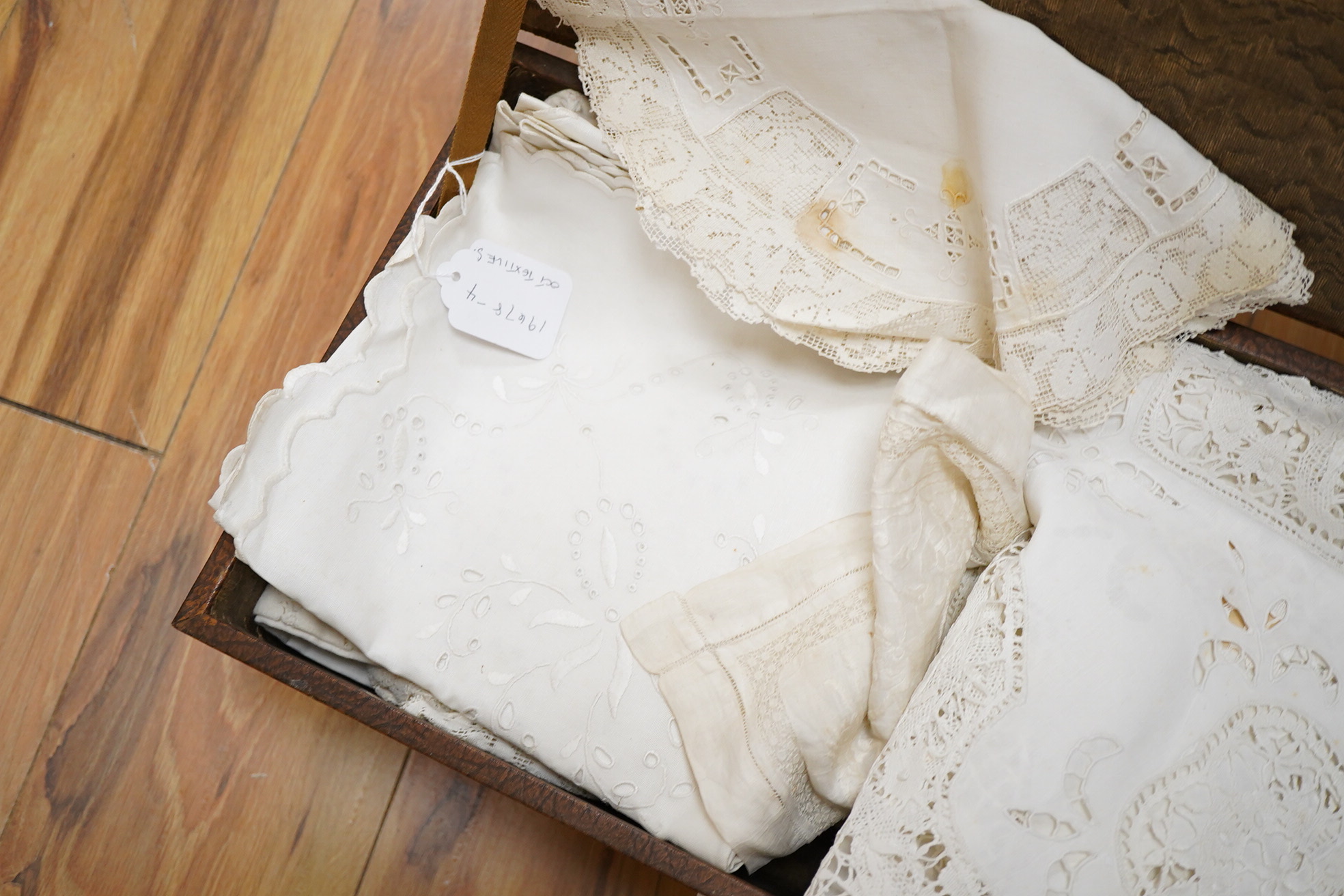 A small box/trunk containing mixed crochet, embroidered anglaise and drawn thread table linens, christening gown, damask cloths and various pieces of lace etc.Ornate circular cloth 112cm diameter. Condition - most need r